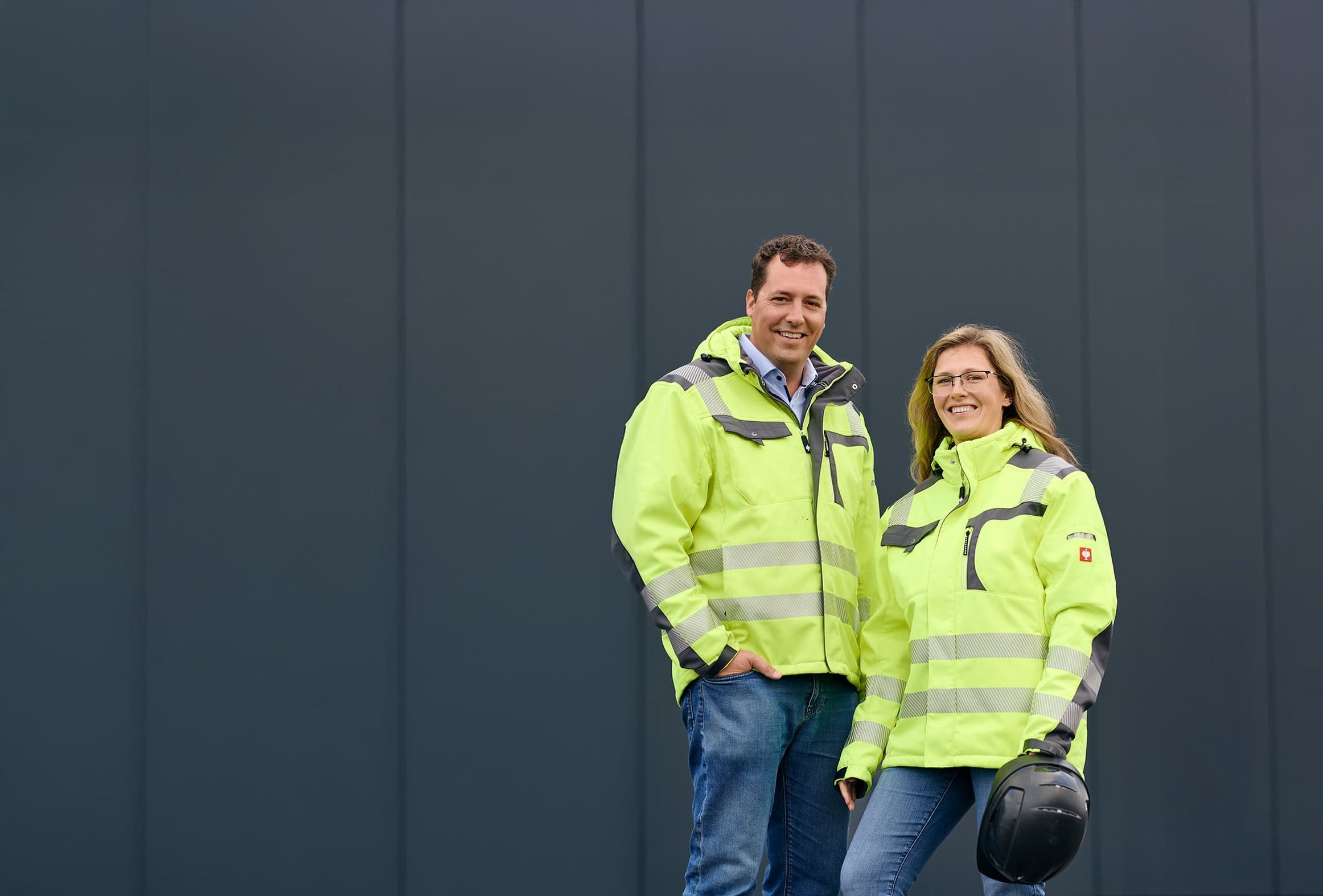 Michelle und Toni Ebeler, nebeneinander in gelber Arbeitskleidung porträtiert.