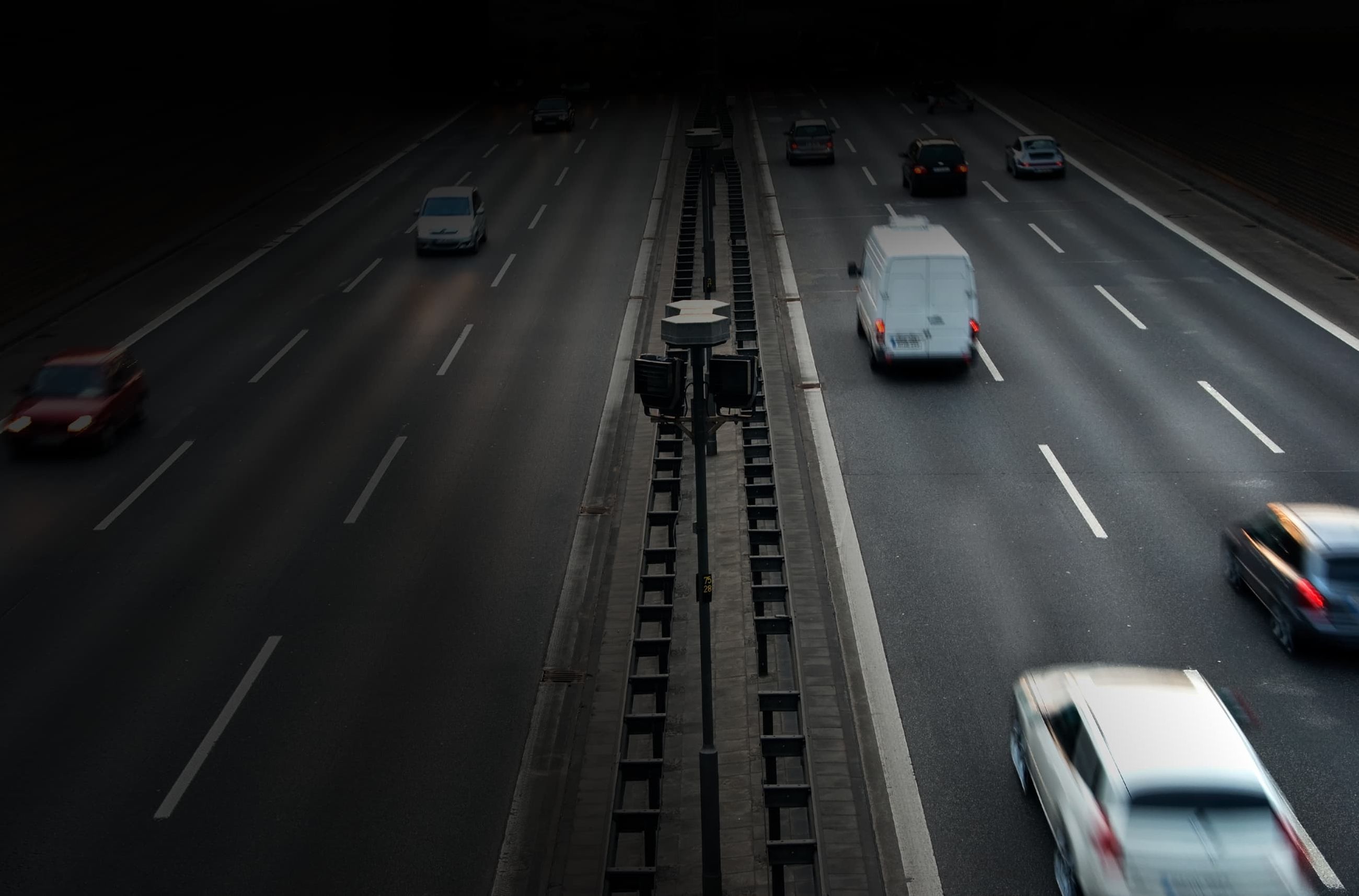 Verkehr auf einer mehrspurigen Straße bei Dämmerung aus der Vogelperspektive mit Scheinwerferlichtern.